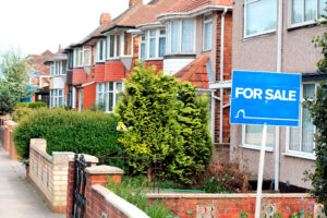 This is an image of a row houses in England with a blue "for sale" sign. The images represents the UK Property Market.